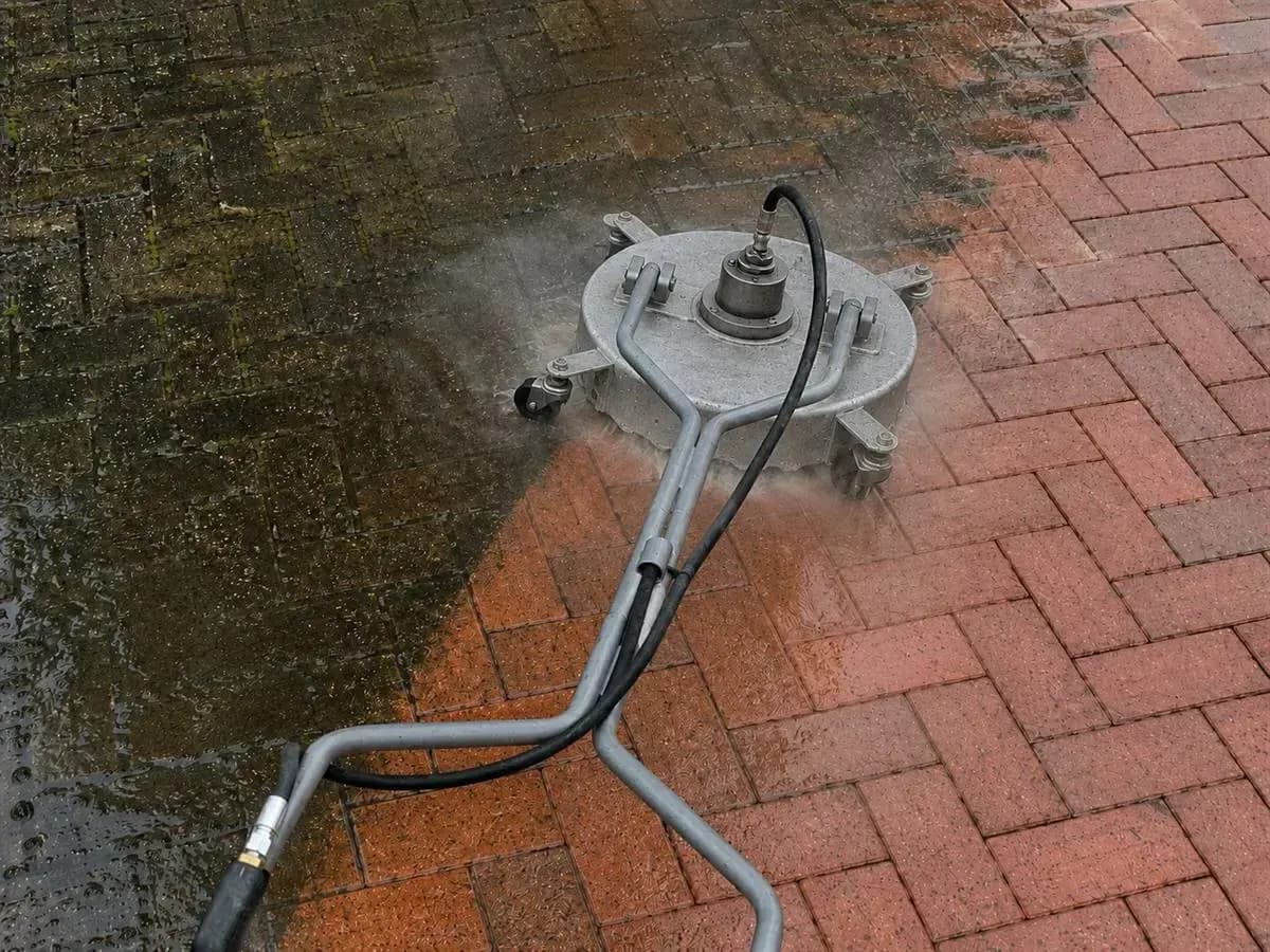 A single block-paved surface mid-clean: mossy, dirty paving on one side and bright restored brick on the other, split by the path of the surface cleaner